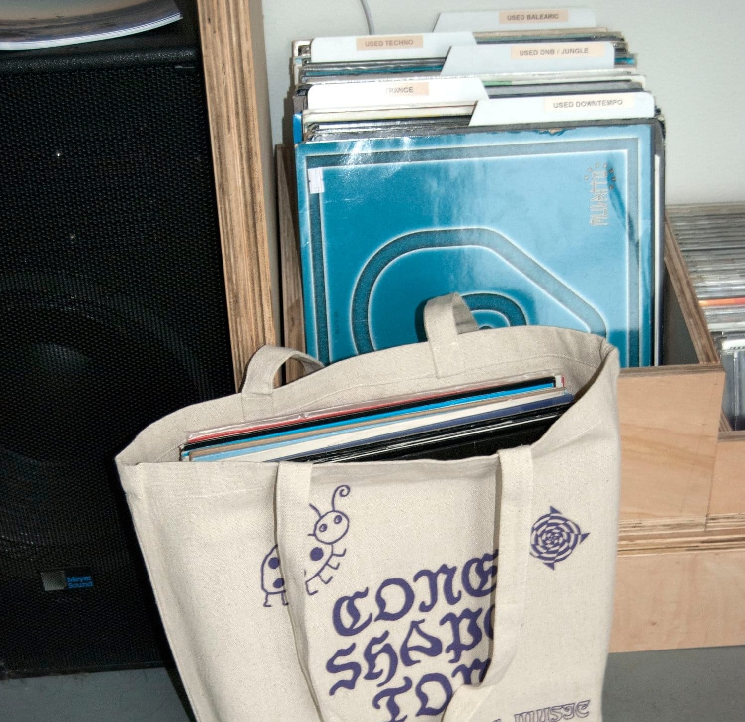 A tote bag with vinyl records in front of bins stocking vinyl records.