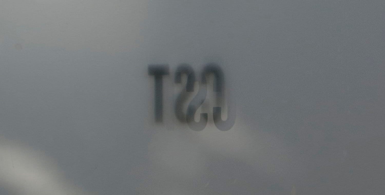 A glass storefront door pictured from the inside looking out bearing the letters "CST," depicted in reverse.